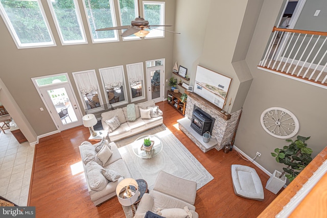 living area featuring ceiling fan, a towering ceiling, baseboards, and wood finished floors