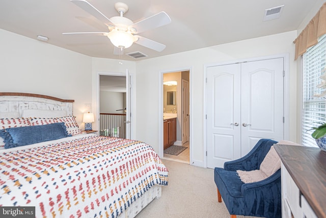 bedroom with a closet, connected bathroom, visible vents, and light colored carpet