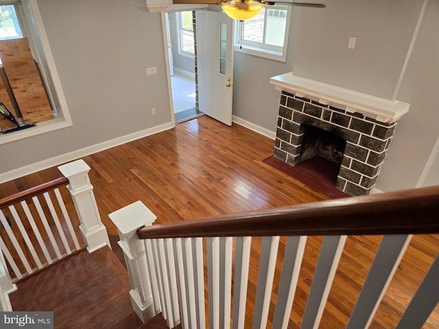 interior space with a healthy amount of sunlight, hardwood / wood-style floors, ceiling fan, and a stone fireplace