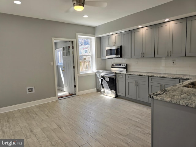 kitchen featuring appliances with stainless steel finishes, tasteful backsplash, ceiling fan, light stone counters, and light wood-type flooring