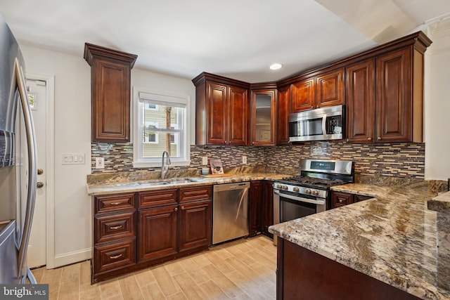 kitchen featuring stainless steel appliances, stone countertops, sink, and light wood-type flooring