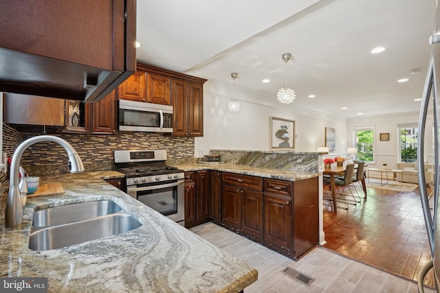 kitchen featuring sink, light stone counters, kitchen peninsula, pendant lighting, and stainless steel appliances