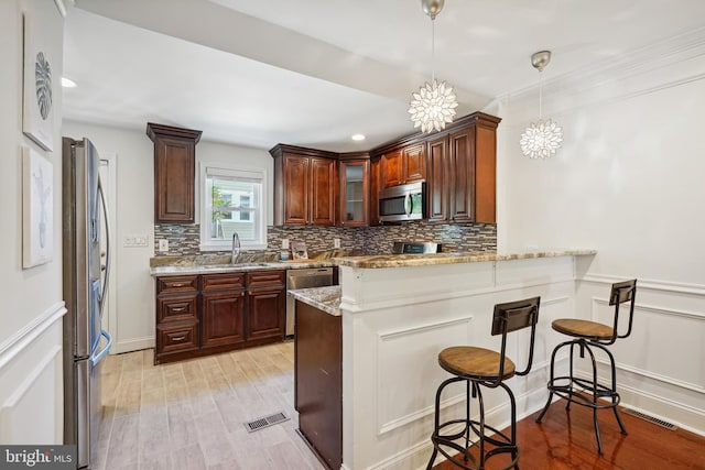 kitchen with pendant lighting, sink, stainless steel appliances, light stone counters, and kitchen peninsula