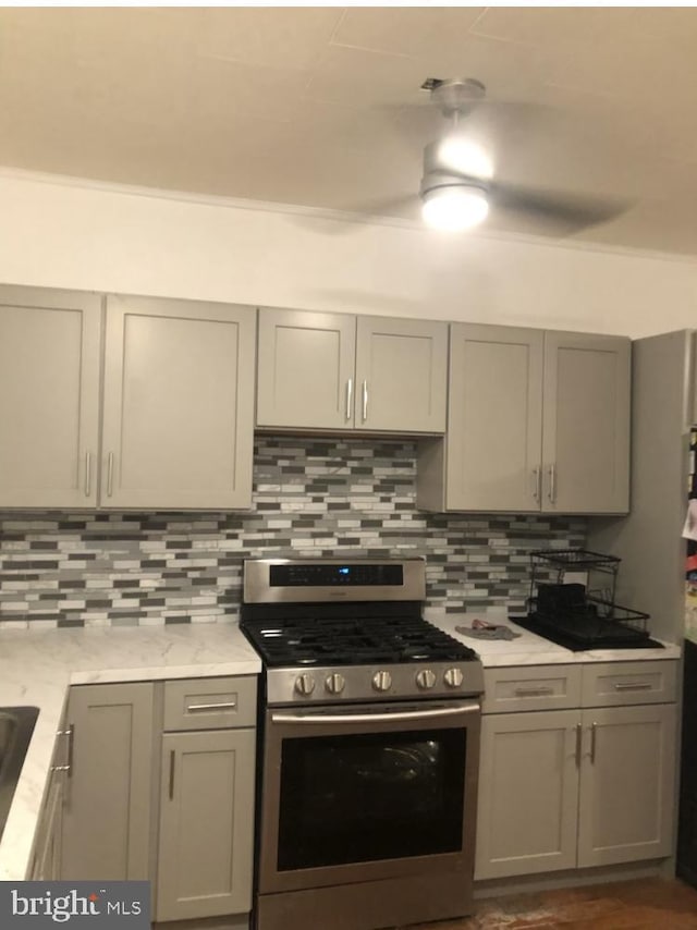 kitchen featuring light stone counters, gas stove, decorative backsplash, and gray cabinetry