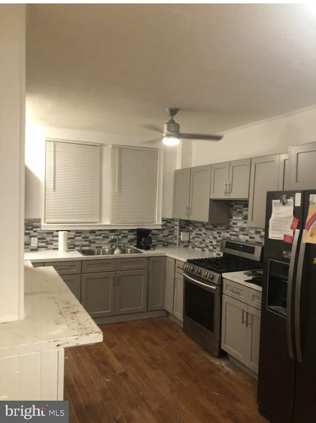 kitchen featuring black fridge with ice dispenser, sink, stainless steel gas stove, dark hardwood / wood-style floors, and backsplash