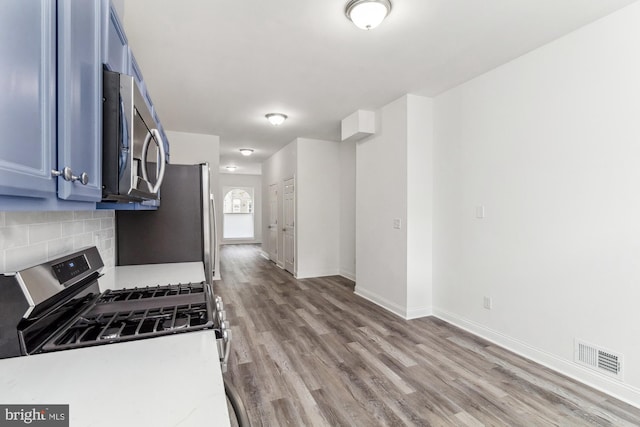 kitchen featuring light wood-type flooring, appliances with stainless steel finishes, blue cabinets, and backsplash