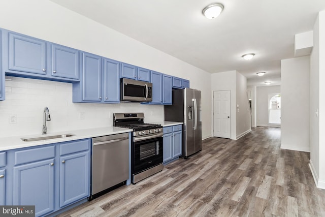 kitchen with blue cabinetry, appliances with stainless steel finishes, light hardwood / wood-style floors, sink, and decorative backsplash