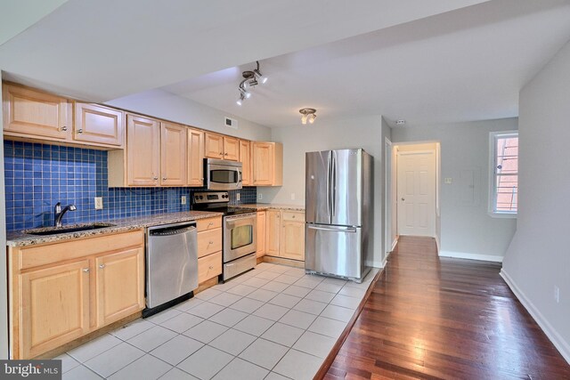 kitchen with light brown cabinets, stainless steel appliances, light hardwood / wood-style floors, sink, and decorative backsplash