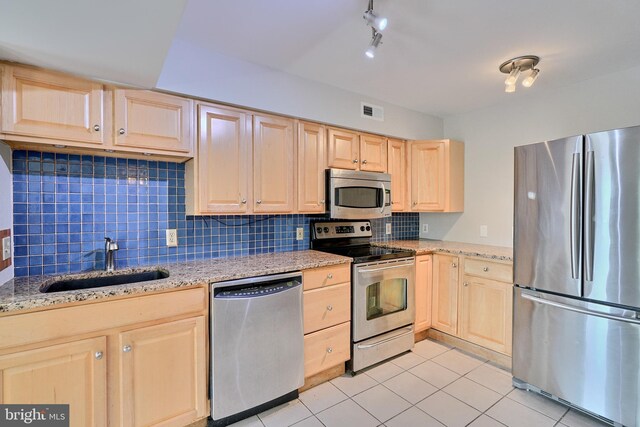 kitchen with appliances with stainless steel finishes, backsplash, rail lighting, and light stone countertops