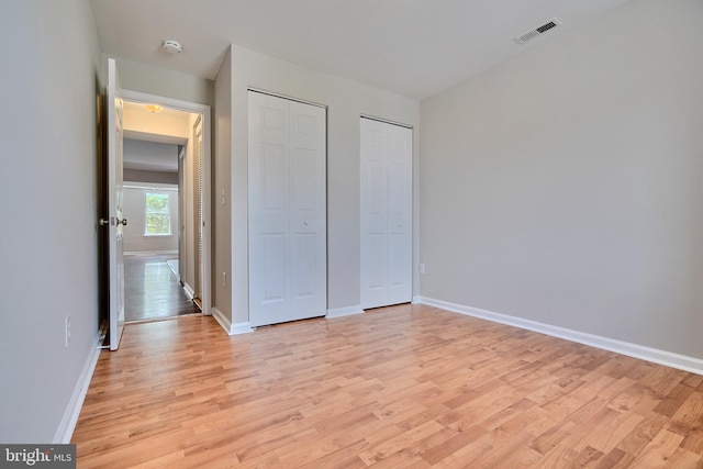 unfurnished bedroom featuring light hardwood / wood-style flooring and multiple closets