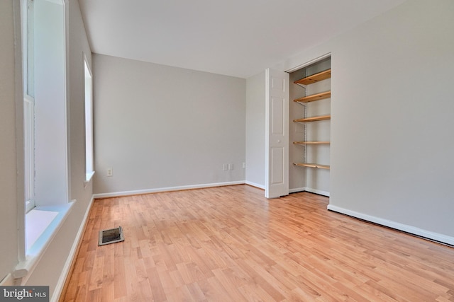 unfurnished room with built in shelves and light hardwood / wood-style flooring