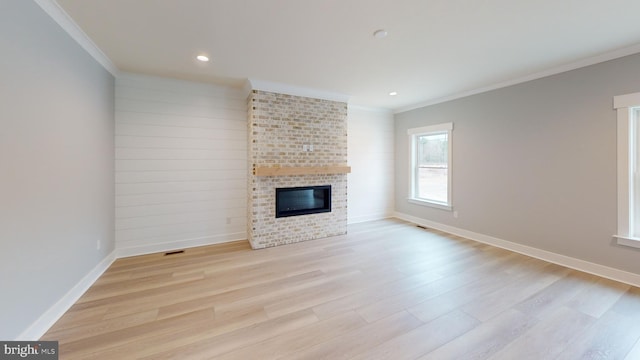 unfurnished living room with ornamental molding, a brick fireplace, and light wood-type flooring