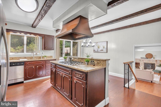 kitchen with hardwood / wood-style floors, stainless steel appliances, a center island, beamed ceiling, and premium range hood