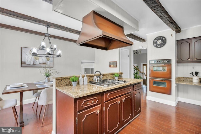 kitchen with light stone countertops, beamed ceiling, premium range hood, stainless steel gas cooktop, and decorative light fixtures