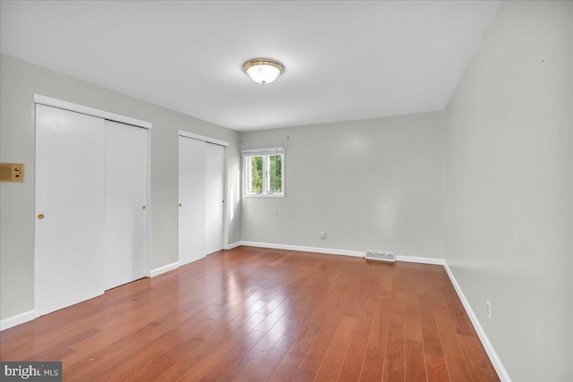 unfurnished bedroom featuring wood-type flooring and two closets