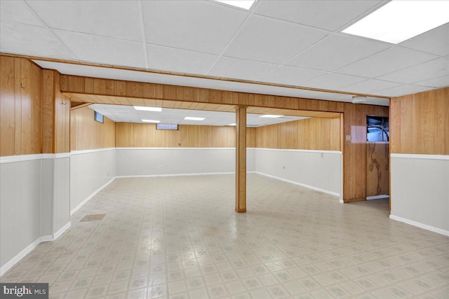 basement featuring wood walls, light tile patterned flooring, and a drop ceiling