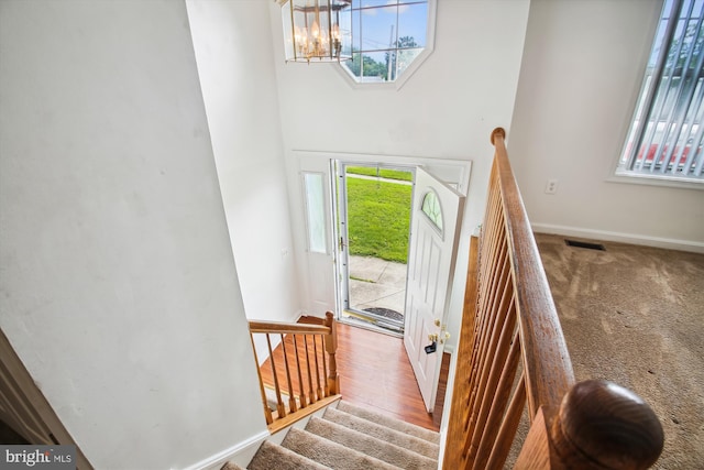 stairway with carpet floors, a wealth of natural light, and a notable chandelier