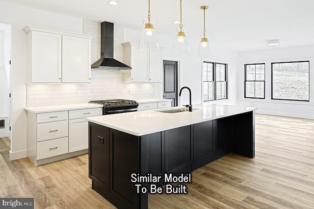 kitchen featuring gas stove, white cabinetry, sink, wall chimney range hood, and a kitchen island with sink