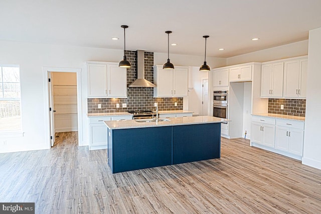 kitchen with hanging light fixtures, wall chimney exhaust hood, white cabinetry, and light hardwood / wood-style floors