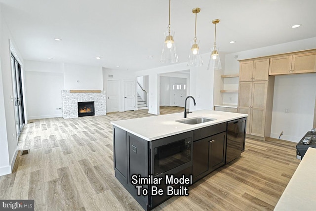 kitchen with light hardwood / wood-style flooring, sink, a stone fireplace, a center island with sink, and light brown cabinets