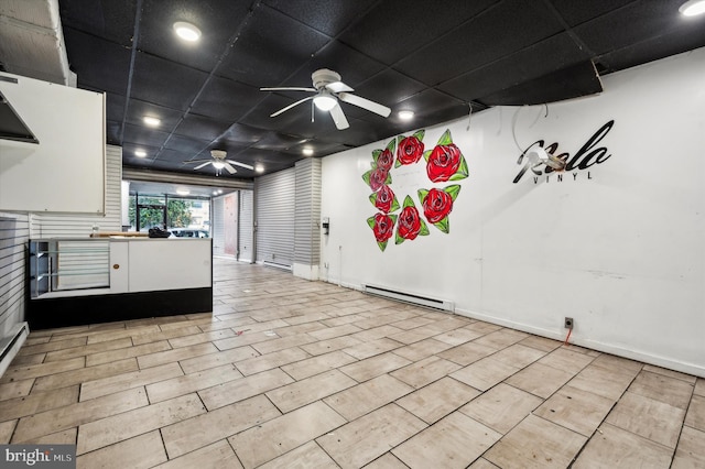 interior space featuring white cabinets, a drop ceiling, a baseboard radiator, and a ceiling fan