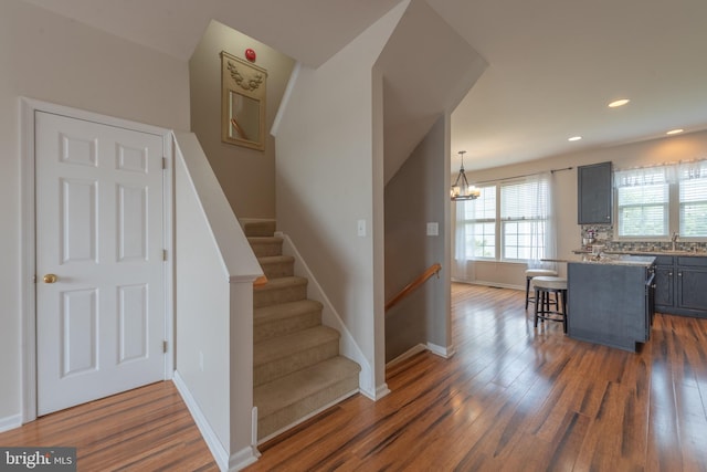 stairway with sink, wood-type flooring, and a notable chandelier