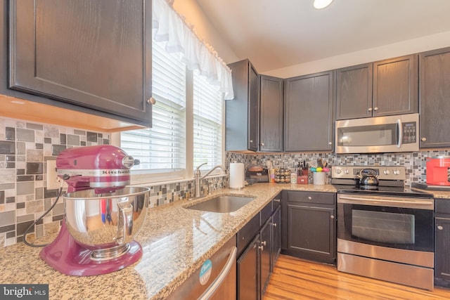 kitchen with light hardwood / wood-style flooring, tasteful backsplash, light stone countertops, sink, and stainless steel appliances