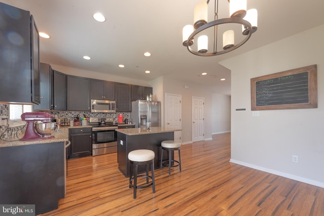 kitchen featuring stainless steel appliances, light hardwood / wood-style floors, light stone counters, a kitchen breakfast bar, and a kitchen island