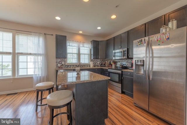 kitchen featuring appliances with stainless steel finishes, light hardwood / wood-style flooring, a wealth of natural light, and light stone countertops