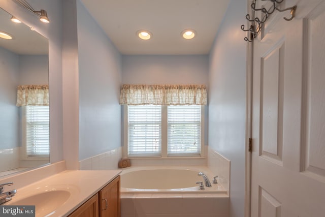 bathroom featuring tiled tub, plenty of natural light, and vanity