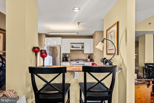 kitchen with a breakfast bar area, appliances with stainless steel finishes, white cabinetry, wood-type flooring, and light stone counters