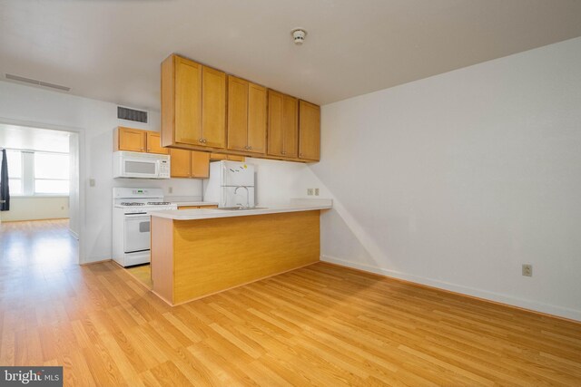 kitchen with light hardwood / wood-style floors, kitchen peninsula, and white appliances