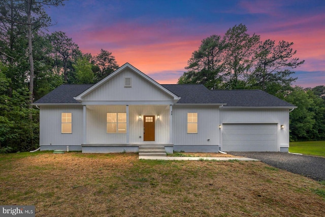 view of front of house featuring covered porch, a garage, a shingled roof, driveway, and a front lawn