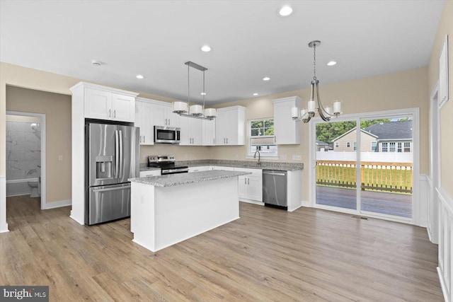 kitchen featuring decorative light fixtures, light wood-type flooring, appliances with stainless steel finishes, a kitchen island, and white cabinets