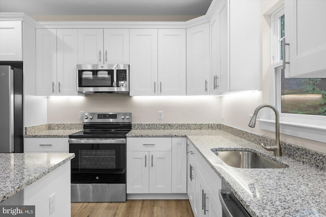 kitchen with light wood-style flooring, appliances with stainless steel finishes, white cabinets, a sink, and light stone countertops