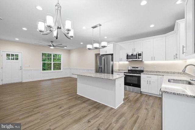 kitchen featuring a center island, a wainscoted wall, appliances with stainless steel finishes, white cabinets, and a sink