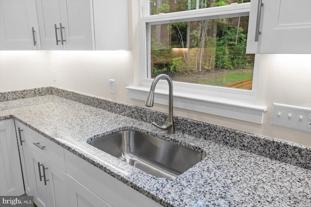 kitchen featuring light stone counters, a sink, and white cabinets