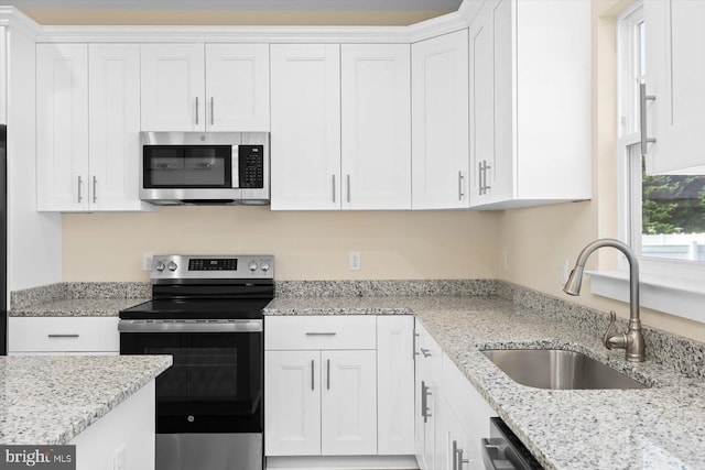 kitchen featuring appliances with stainless steel finishes, white cabinetry, sink, and light stone countertops