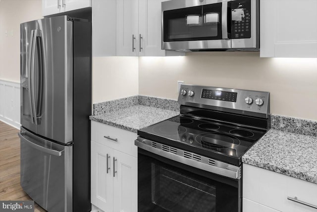 kitchen with appliances with stainless steel finishes, light stone counters, and white cabinets