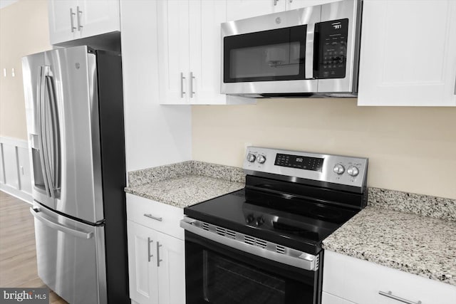 kitchen with white cabinets, light wood-type flooring, light stone counters, and stainless steel appliances