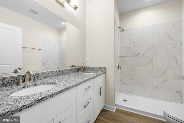 full bath with a sink, a tile shower, toilet, and wood finished floors