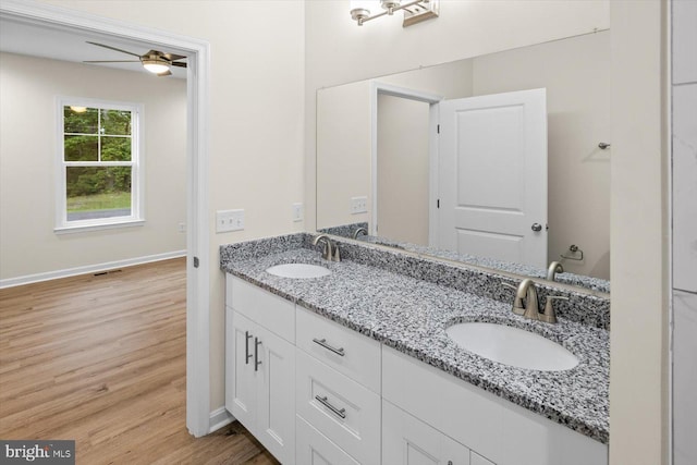 full bath featuring double vanity, wood finished floors, a sink, and baseboards