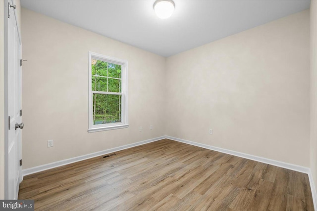 empty room with wood finished floors, visible vents, and baseboards