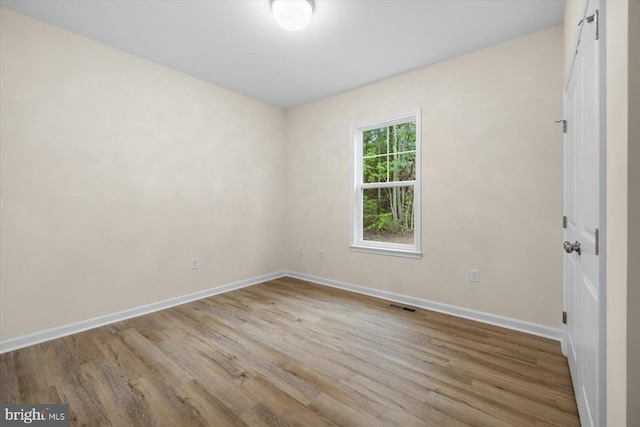 unfurnished room featuring wood finished floors, visible vents, and baseboards