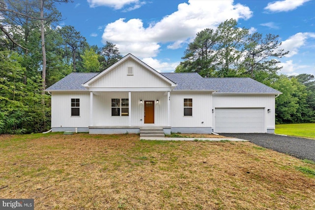 modern farmhouse featuring covered porch, a shingled roof, a front yard, and an attached garage