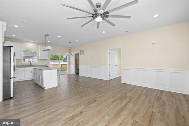 kitchen with light hardwood / wood-style floors, stainless steel refrigerator, white cabinets, a kitchen island, and hanging light fixtures