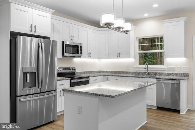 kitchen featuring stainless steel appliances, a kitchen island, a sink, light wood-style floors, and white cabinets