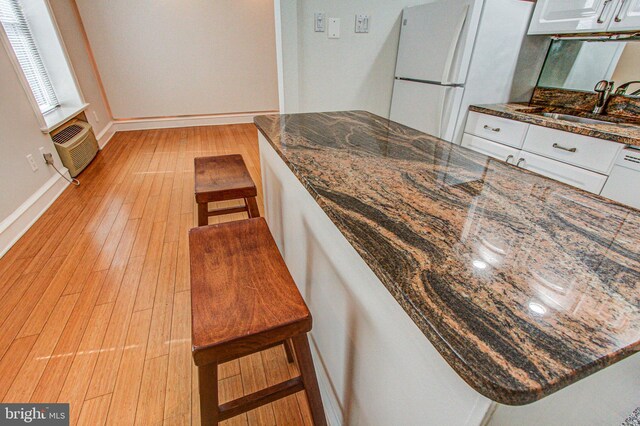 kitchen with white refrigerator, white cabinets, light wood-type flooring, sink, and dark stone countertops