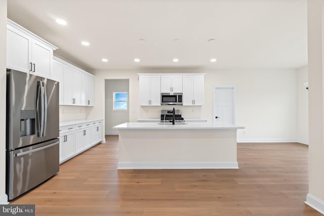 kitchen with white cabinetry, stainless steel appliances, and a center island with sink