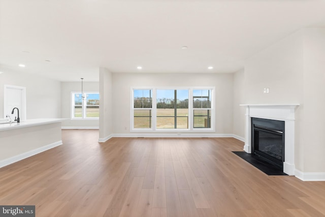 unfurnished living room with an inviting chandelier, a wealth of natural light, sink, and light hardwood / wood-style flooring